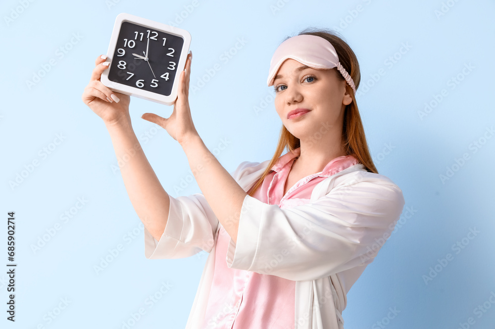 Young woman in pajamas with clock on blue background
