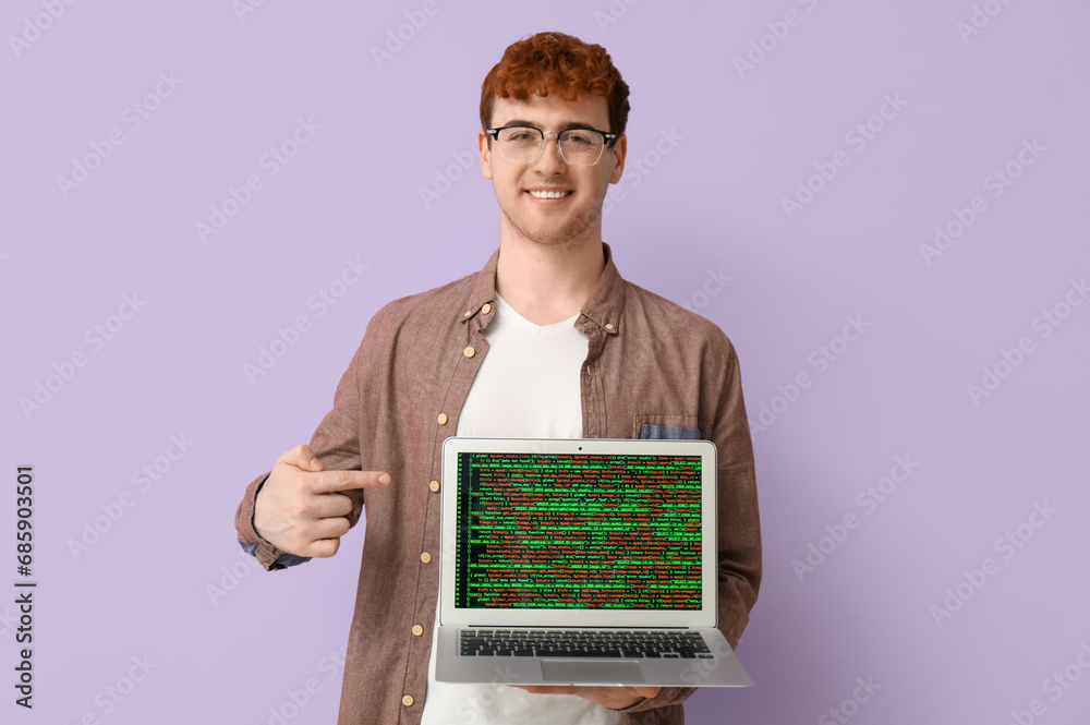 Male programmer pointing at laptop on lilac background