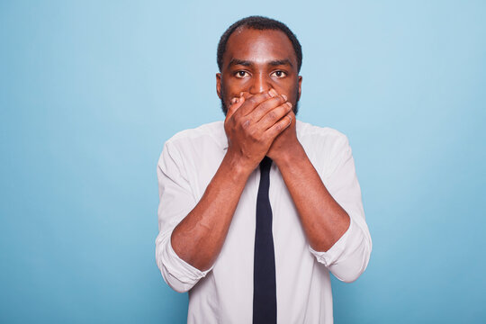 Terrified shocked black man keeps hands on his mouth and cannot believe something. Young individual feeling surprised after sharing a secret by mistake. Person mistakenly gossiped.