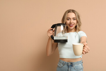 Poster - Beautiful young woman with modern electric kettle and cup on beige background