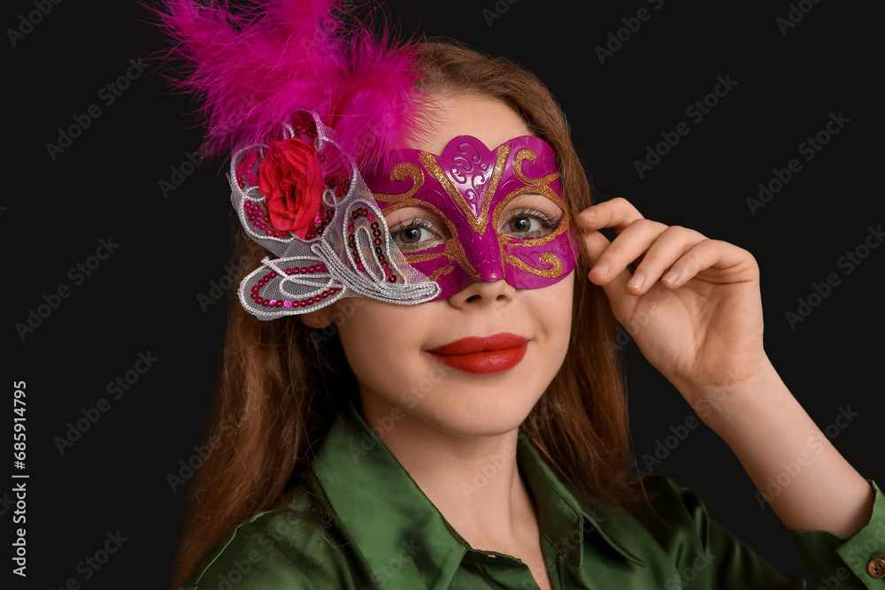Beautiful young woman in carnival mask on black background