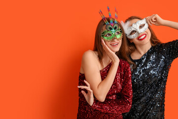 Happy young women in carnival masks on orange background