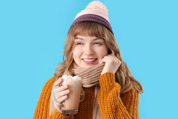 Canvas Print - Pretty young woman holding cup of hot chocolate with marshmallows on blue background