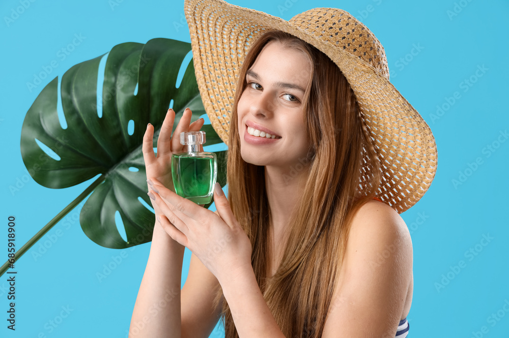 Young woman in straw hat with perfume and palm leaf on blue background