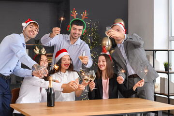 Canvas Print - Young coworkers with sparklers and champagne celebrating New Year at corporate party in office