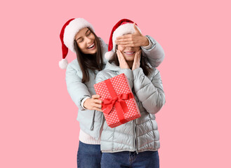 Sticker - Young woman surprising her friend with Christmas gift on pink background