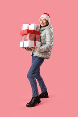 Wall Mural - Young woman in Santa hat with Christmas gifts on pink background