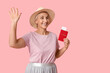 © Pixel-Shot - Mature woman with passport waving hand on pink background. Travel concept