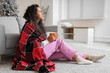 Beautiful young African-American woman with cup of hot mulled wine on carpet at home