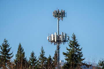 Mobility communications cell site tower with two layers of antennas standing out above the tree line on sunny winter day
