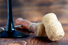 Two Wine Corks Close-up, Corkscrew And Glass Legs In The Background, On A Wooden Background