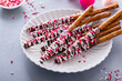 Chocolate dipped pretzel rods with pink heart sprinkles on a plate