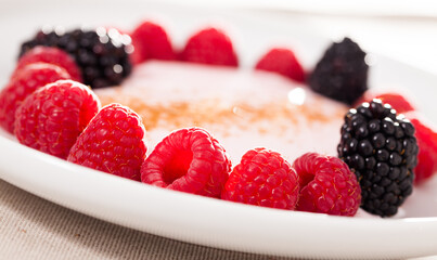 Wall Mural - Raspberries and blackberries laid out on a white plate in circle with yogurt and cinnamon