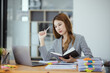 © SOMKID - Businesswoman working with stack of documents papers and laptop sitting at office desk.