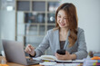 © SOMKID - Accounting asian woman use smartphone and laptop at office desk in office, Accounting businesswoman online working concept.