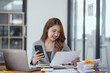 © SOMKID - Accounting asian woman use smartphone and laptop at office desk in office, Accounting businesswoman online working concept.