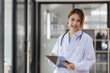 © SOMKID - Happy asian female doctor holding a patient clipboard standing in hospital, Medicine and healthcare concept.