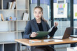 © SOMKID - Asian businesswoman working on laptop and financial document paper sitting at desk in office workplace.