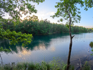 The image showcases a tranquil lakeside scene during the magical hours of twilight. The calm waters reflect the waning light and colors of the sky, while trees hug the shoreline, their leaves a