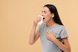 Suffering from allergy. Young woman blowing her nose in tissue on beige background. Space for text