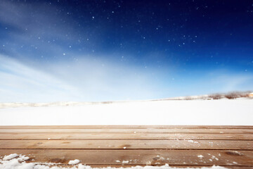 Poster - Wooden floor against snowy landscape under blue sky with snowflakes. High quality photo