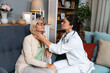 During a home visit to an elderly patient, a young endocrinologist doctor checks her thyroid gland by feeling her neck with her hands. Senior women endocrinology health care