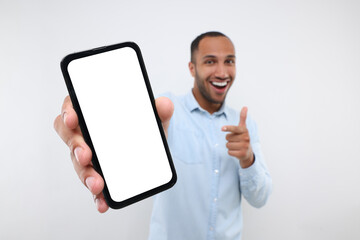 Sticker - Young man showing smartphone in hand and pointing at it on white background, selective focus. Mockup for design