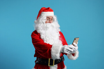 Canvas Print - Merry Christmas. Santa Claus using smartphone on light blue background