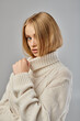 © LIGHTFIELD STUDIOS - beautiful blonde woman in white winter sweater looking at camera on grey, sophisticated beauty