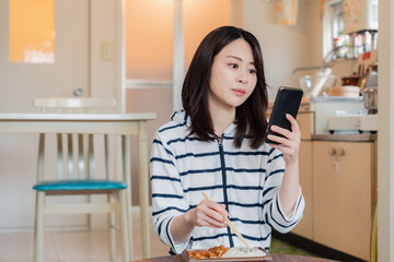 Wall Mural - スマホを使いながら家でコンビニ弁当を食べる若い女性