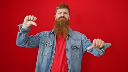 Poster - Cool, bearded redhead guy giving thumbs down — a negative sign of failure in casual lifestyle fashion, standing over an isolated red wall