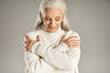© LIGHTFIELD STUDIOS - attractive and grey haired middle aged woman in white winter outfit standing grey background