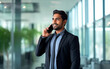 © GustavsMD - Happy Indian business man talking on mobile cell phone device looking away standing at work. Smiling professional businessman making call on smartphone working with cellphone in office.