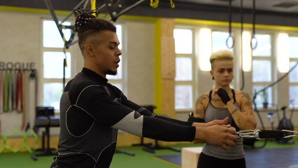 Wall Mural - Male sport coach explaining to young woman how to training with cable crossover machine at gym. Attractive woman working out with personal coach.