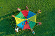 © New Africa - Group of children and teachers playing with rainbow playground parachute on green grass, top view. Summer camp activity
