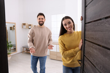 Happy couple welcoming at home. Invitation to come indoors