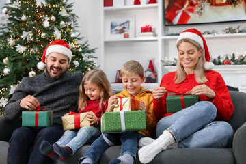 Poster - Happy family in Santa hats with Christmas gifts on sofa at home