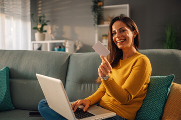 Happy woman is showing credit card while shopping online on laptop form home.