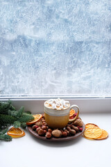 Wall Mural - cocoa mug with marshmallows, dried orange slices, nuts, fir branches on windowsill. New year and Christmas holidays background. festive winter season. home hygge comfort in cold weather