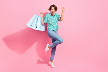 Wall Mural - Full body photo of delighted pretty lady hold store bags raise fist empty space isolated on pink color background
