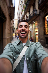 Wall Mural - Happy vertical selfie of a young caucasian man in an old town of Barcelona. Male tourist taking a self portrait using smartphone to post it on social media,