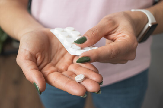 young woman holding pill in a hand, painkiller or antibiotic, taking medicine from blister pack, clo
