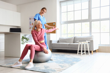 Wall Mural - Female physiotherapist working with mature woman on fitball in rehabilitation center