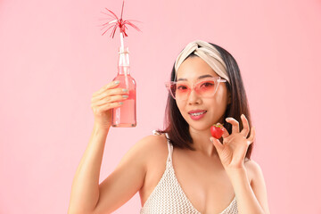 Wall Mural - Beautiful Asian woman in swimsuit and with strawberry drink on pink background