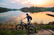 © Sergei Dvornikov - Man with an electric fatbike on the background of a lake and sunset. Picturesque place in the village. Concept of a healthy lifestyle.