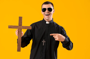 Wall Mural - cool priest pointing at cross on yellow background