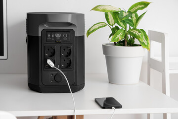 Wall Mural - Mobile phone charging from portable power station on white table, closeup