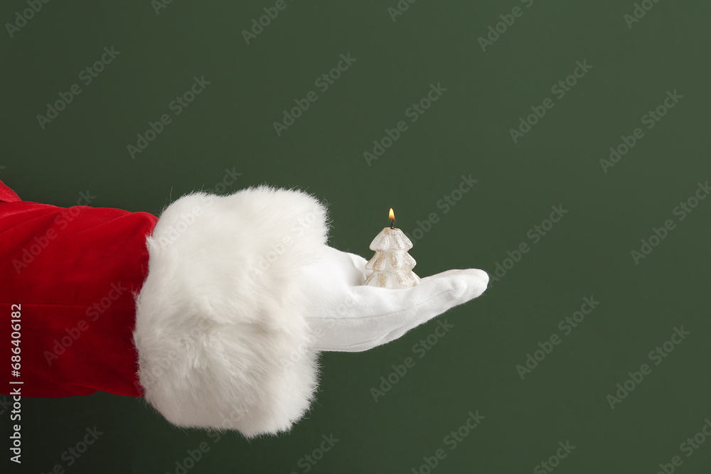 Santa hand with burning candle on green background, closeup