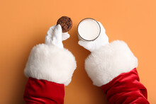 Santa Hands With Glass Of Milk And Cookie On Color Background, Closeup