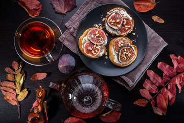 Wall Mural - Toast with cream cheese, fig slices, pine nuts, sunflower seeds and sesame seeds on a plate. Hot tea in a cup and teapot on a dark table